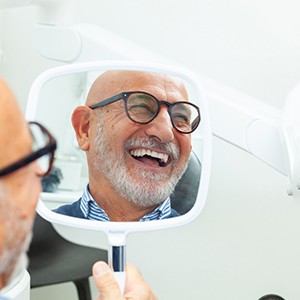 Man with glasses smiling at reflection in handheld mirror