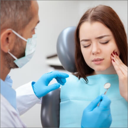 Woman holding cheek during appointment with emergency dentist