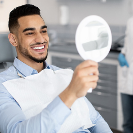 Man smiling at reflection in handheld mirror