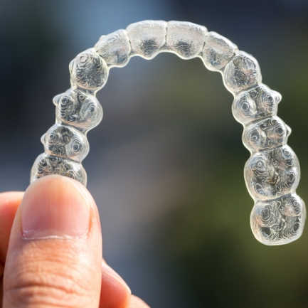 Hand holding an Invisalign aligner tray