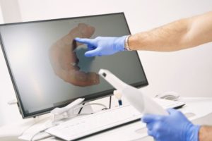Dentist holding digital scanner, pointing at computer monitor
