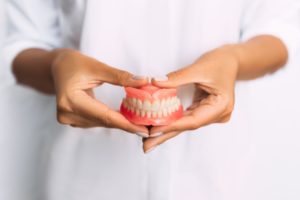 Woman in white holding dentures with two hands in front of her